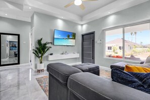 A modern living room with a large window, a flat-screen TV, and a grey sectional sofa.