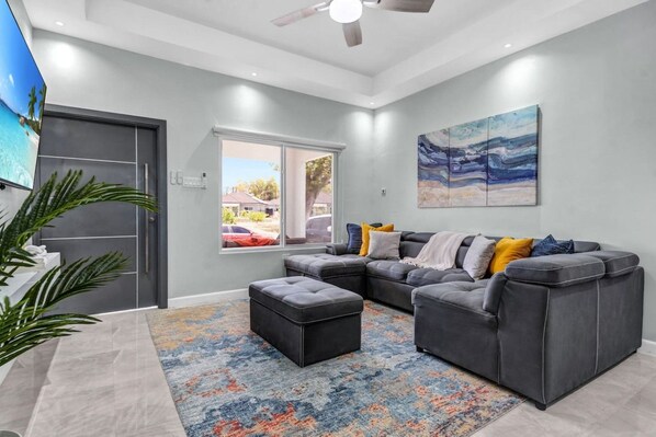 A modern living room with a sectional sofa, ottoman, and a colorful rug.