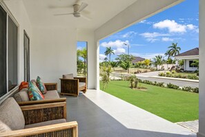 A spacious balcony with a ceiling fan, a seating area with cushions, and a view of a well-maintained lawn and neighboring houses.
