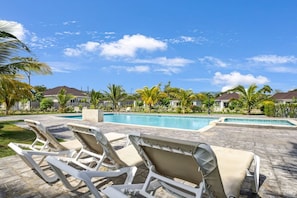 Zona de piscina con sillones de descanso, una piscina y vistas a casas al fondo.
