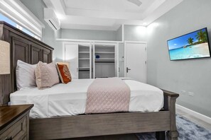 A bedroom with a bed, a wardrobe, a television, and a window with a view of the beach.