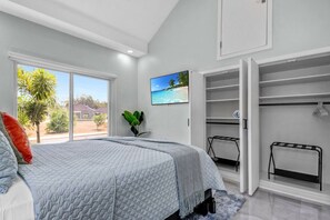A bedroom with a bed, a large window, a closet, and a wall-mounted TV.