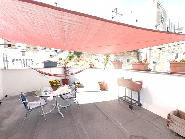 A rooftop terrace with a table and chairs, potted plants, and a red shade sail. - House across from the castle offering a charming vacation experience in Massafra (Massafra)