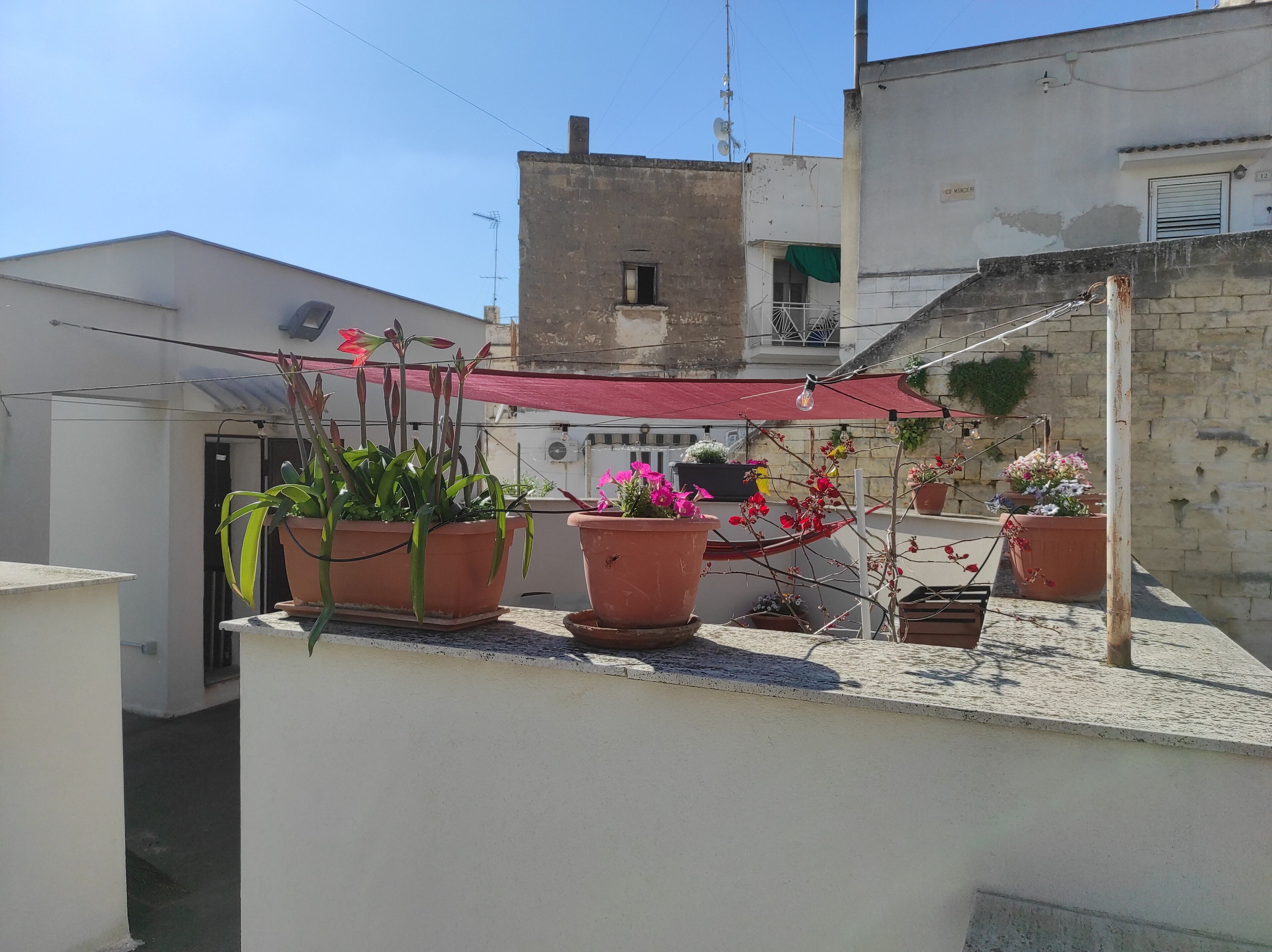 Una terraza en la azotea con plantas en macetas y un toldo rojo.