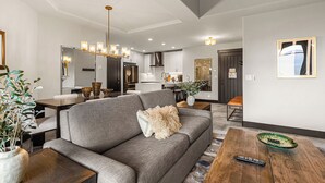 A modern living room with a grey sofa, wooden coffee table, and a dining area with a dark wooden table.