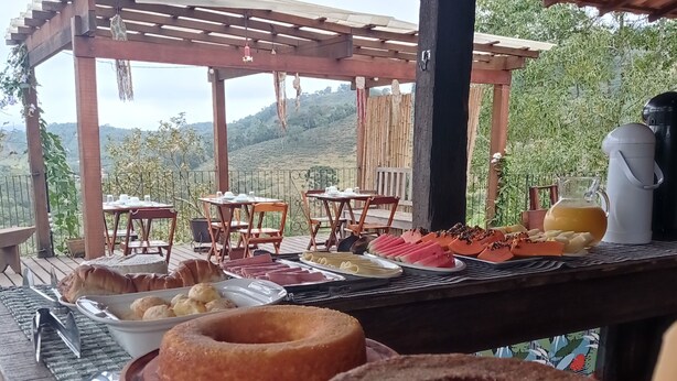 A covered outdoor dining area with tables set for a meal, featuring a scenic view of hills in the background. - Casa do Geninho Pousada e Camping  (Lima Duarte)