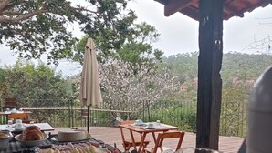 An outdoor dining area with a table set for breakfast, including fruits, pastries, and a beverage pitcher. - Casa do Geninho Pousada e Camping  (Lima Duarte)