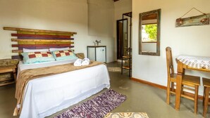 A bedroom with a wooden headboard, a bed with white bedding, a small table with a lace tablecloth, and a mirror on the wall. - Casa do Geninho Pousada e Camping  (Lima Duarte)