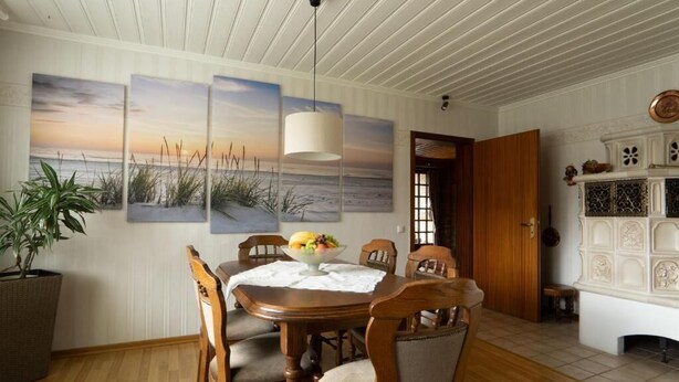 A dining area with a wooden table, chairs, and a bowl of fruit. There are three paintings on the wall depicting a beach scene.