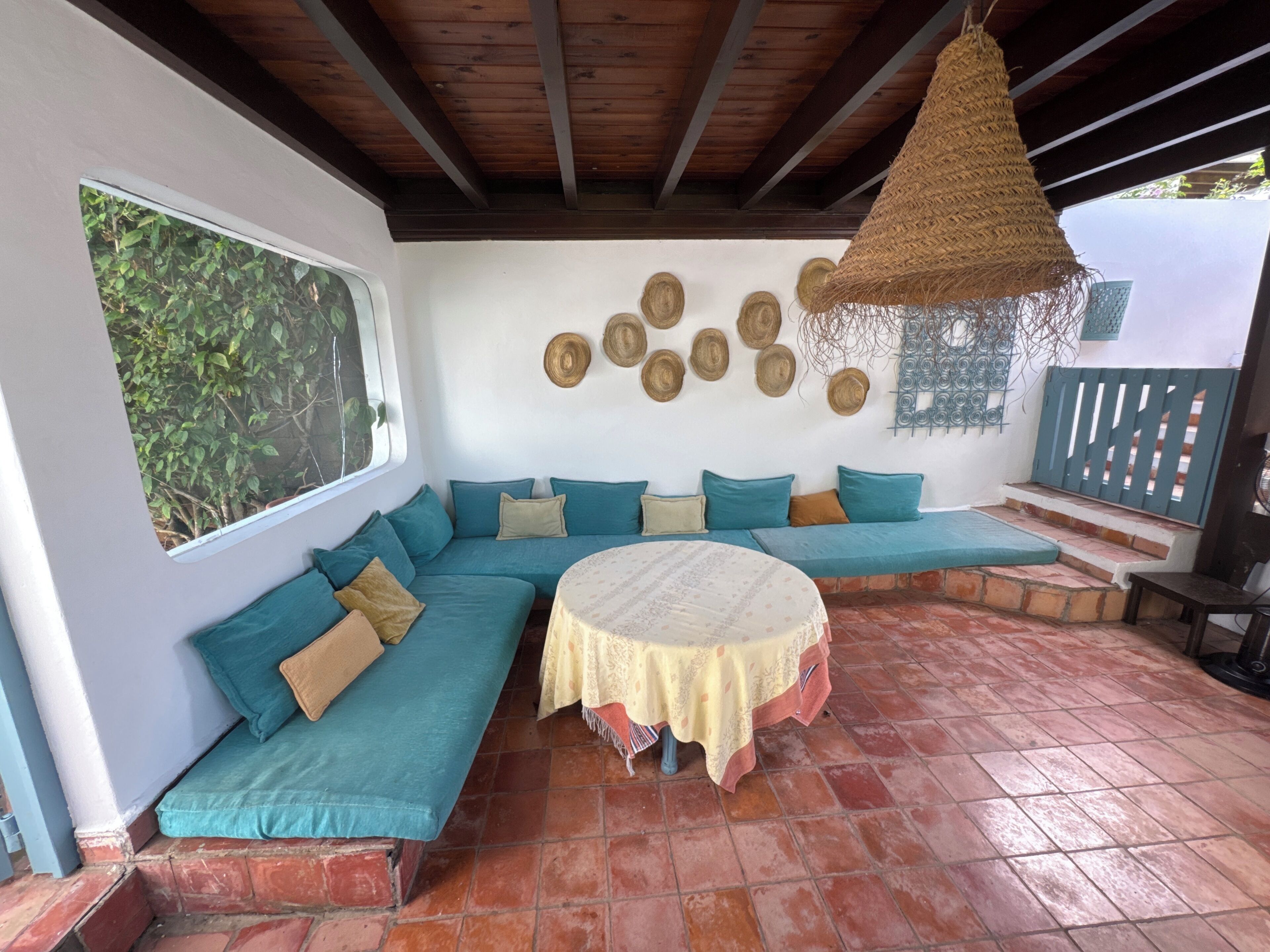 Un espacio de estar al aire libre techado con una mesa redonda, una lámpara colgante tejida y una pared decorada con adornos circulares.