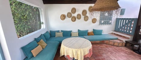 A covered outdoor seating area with a round table, a woven hanging light fixture, and a wall decorated with circular wall hangings.