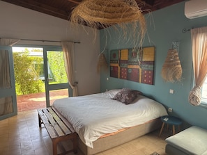 Ein Schlafzimmer mit einem Bett, einer Bank, einem kleinen Hocker und einer Wanddeko aus Makramee.