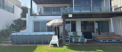 Una casa moderna de dos pisos con un porche cubierto, piscina y mobiliario de exterior.