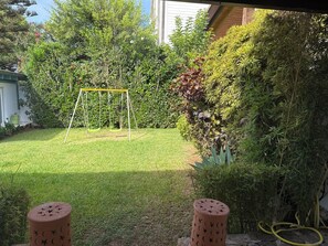 Ein Garten mit Schaukel, Gartenschlauch und verschiedenen Pflanzen.
