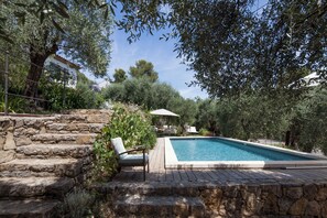 Un escalier en pierre mène à un espace piscine équipé d’une chaise et d’un parasol.