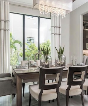 A modern dining area with a large window, a chandelier, and a table set for four.
