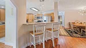 Una cocina moderna con armarios de madera, una isla central y un comedor con sillas blancas y una mesa de madera.