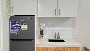 Une cuisine équipée d’un réfrigérateur, de meubles blancs, d’un plan de travail en bois et d’un petit évier.