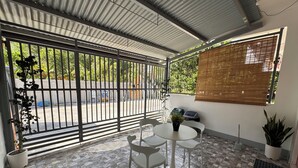 Un patio couvert doté d’un sol carrelé en pierre, d’une table ronde avec des chaises et de plantes en pot.