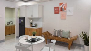 Une cuisine moderne avec des meubles blancs, un réfrigérateur noir et un évier. On y trouve également un coin repas avec une table ronde, des chaises blanches et un banc avec des coussins.