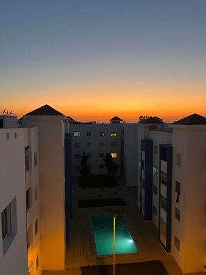 A courtyard with a swimming pool, surrounded by modern buildings with flat roofs and multiple windows. - Cozy Apartment with Pool (Assilah)