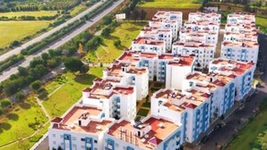 A modern apartment complex with multiple buildings, a central courtyard, and a highway in the background.