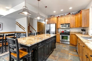 Cocina moderna con encimeras de granito, armarios de madera y electrodomésticos de acero inoxidable, además de una isla central con taburetes de bar.