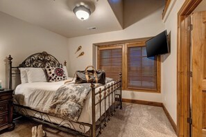 Ein Schlafzimmer mit einem Bett, einem Fernseher, einer Holztür und einem Fenster mit Jalousien.