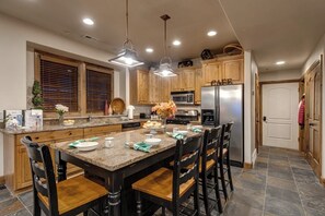 Eine Küche mit Holzausstattung, einer Granit-Arbeitsplatte, einem Edelstahl-Kühlschrank und einem Essbereich mit einem Marmor-Tisch und Holzstühlen.