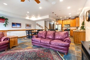A spacious living room with a purple leather sofa, a dining area with a wooden table and chairs, a kitchen with wooden cabinets and modern appliances, and a staircase leading to another level.