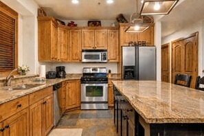 A kitchen with wooden cabinets, a stainless steel refrigerator, a microwave, a stove, and a granite countertop.