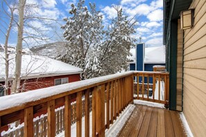 A wooden deck with a railing, a snow-covered tree, and a building with a blue facade.