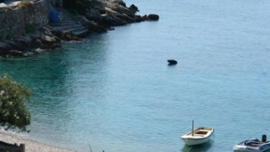 A coastal scene with a rocky shoreline, a small boat, and a larger boat anchored near the shore.