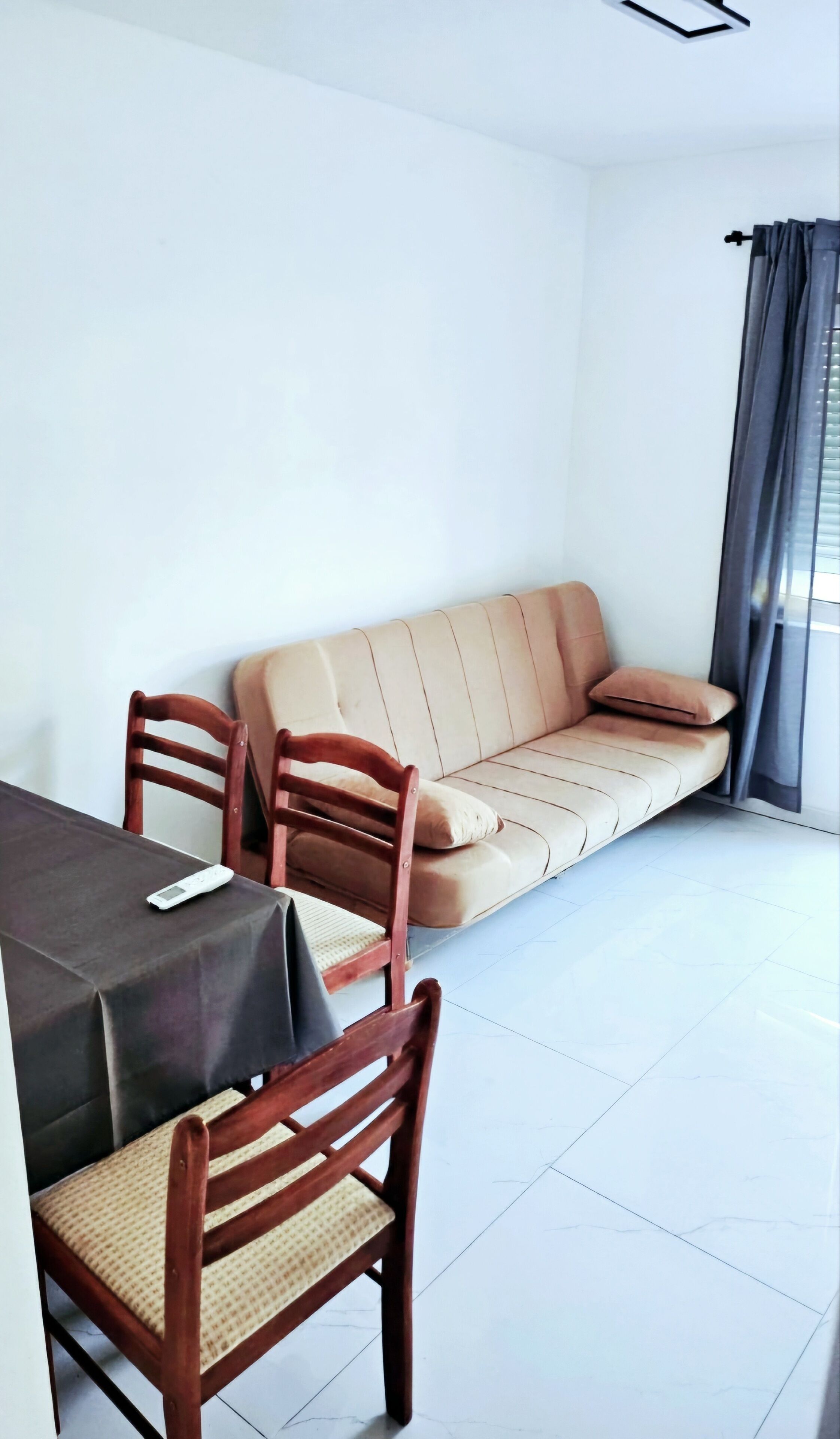A modern living room with a beige sofa, two wooden chairs, a small table, and a window with curtains.