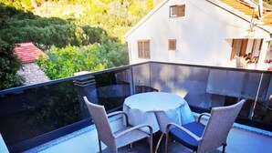 A balcony with a table and chairs, overlooking a mountainous landscape.