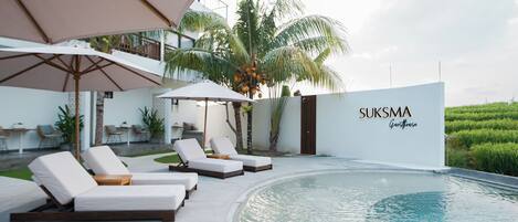 A modern pool area with lounge chairs and umbrellas, a palm tree, and a sign reading "SUKSMA".