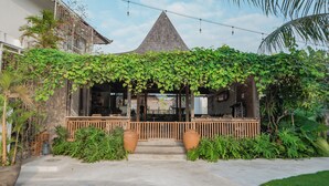 A building with a sloped roof, a wooden porch, and a covered entrance area with a railing. - Suksma Guesthouse (Tumbak Bayuh)
