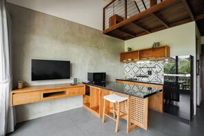 A modern kitchen with a flat-screen TV, wooden cabinetry, a black refrigerator, and a patterned backsplash. - Suksma Guesthouse (Tumbak Bayuh)