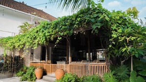 A house with a covered porch, large potted plants, and a wooden fence. - Suksma Guesthouse (Tumbak Bayuh)