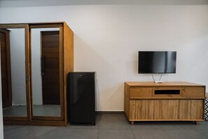 A room with a sliding wooden door, a black refrigerator, a wooden cabinet with a TV on top, and a patterned rug. - Suksma Guesthouse (Tumbak Bayuh)