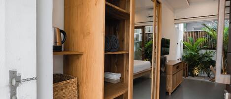 A modern room with a wooden wardrobe, a bed, a TV, and a small kitchen area.