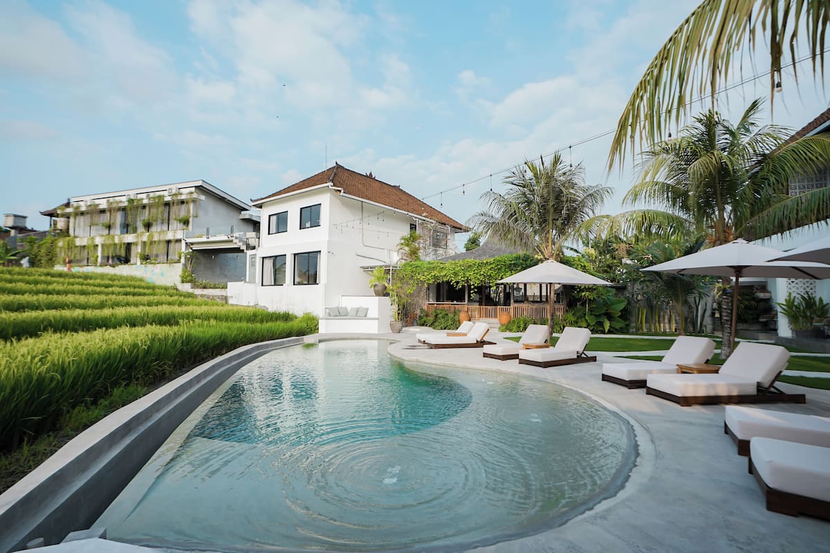 A swimming pool with lounge chairs, a white house, and lush greenery.