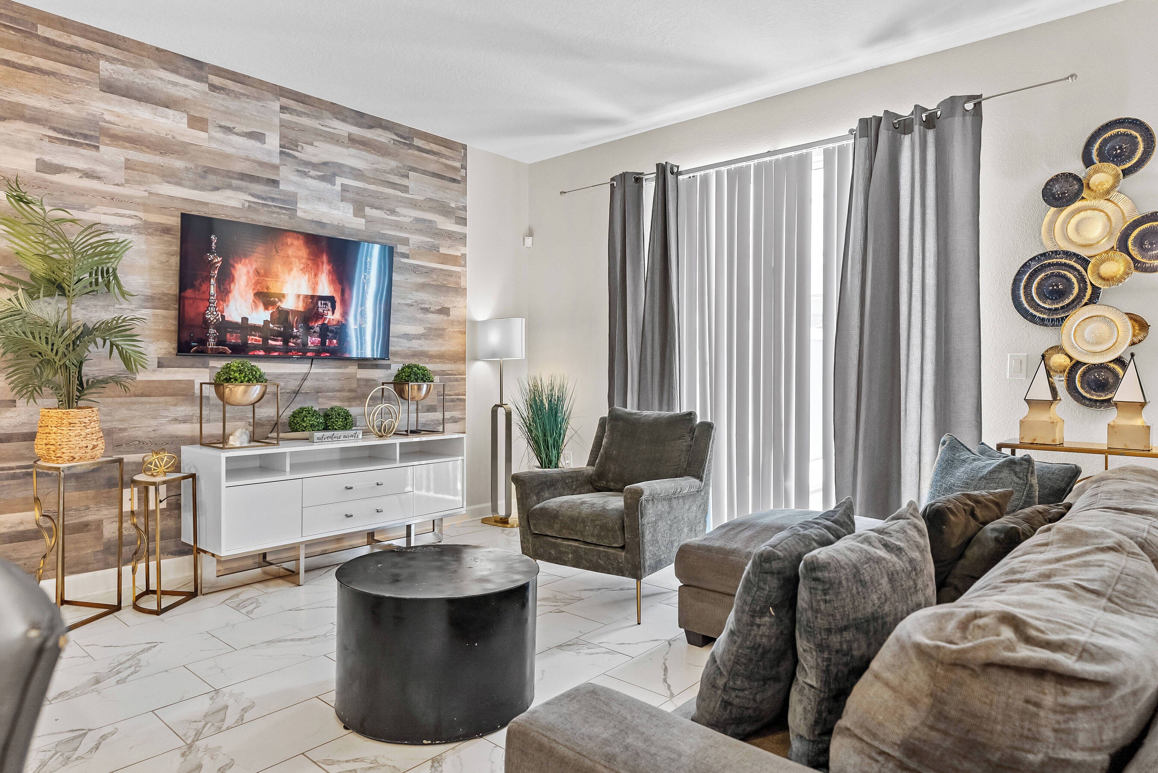 Uma sala de estar moderna com televisão de tela plana, cortinas cinzas, um sofá cinza, um armário branco e pratos decorativos na parede.