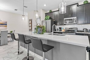 Uma cozinha moderna com armários escuros, eletrodomésticos de aço inoxidável e uma ilha central com banquetas.