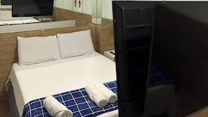 Et hotelværelse med seng, fjernsyn, klimaanlæg og et badeværelsesspejl.