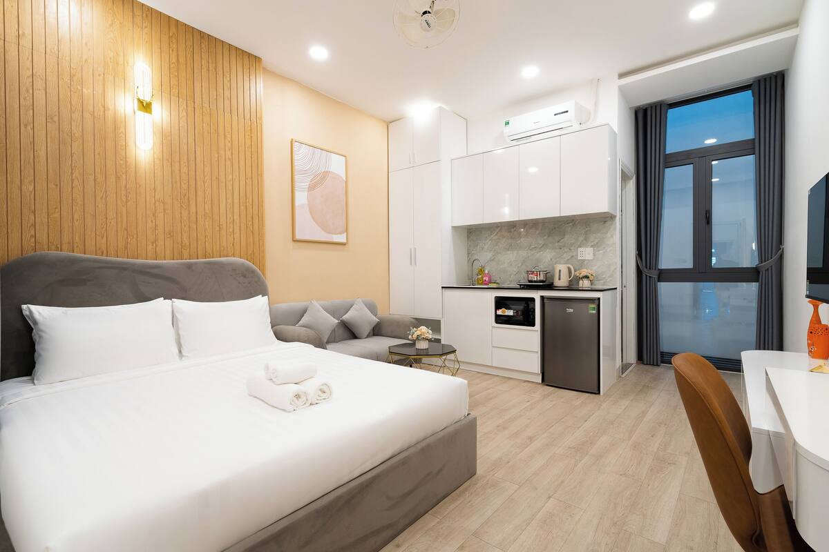 Una habitación de hotel moderna con una cama grande, un sofá, una pequeña cocina y una mesa de comedor.