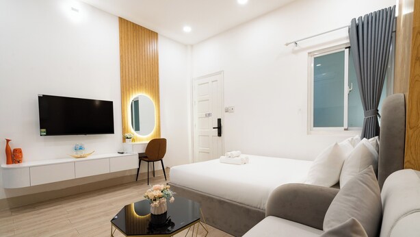 Una habitación de hotel moderna con televisión de pantalla plana, un tocador con espejo, una cama con vistas al exterior, un sofá y una mesita con un jarrón de flores.