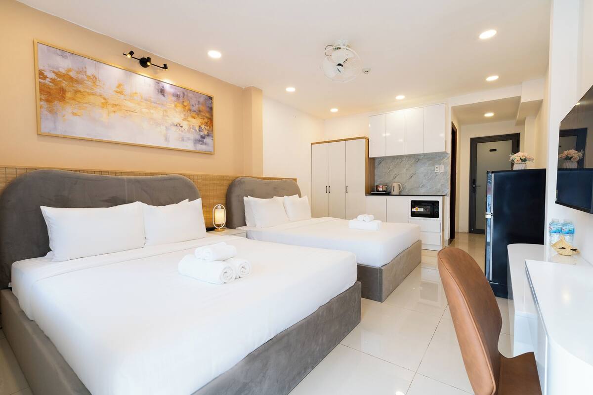 Habitación de hotel con dos camas, una mesa de comedor, una zona de cocina y un cuadro abstracto grande en la pared.