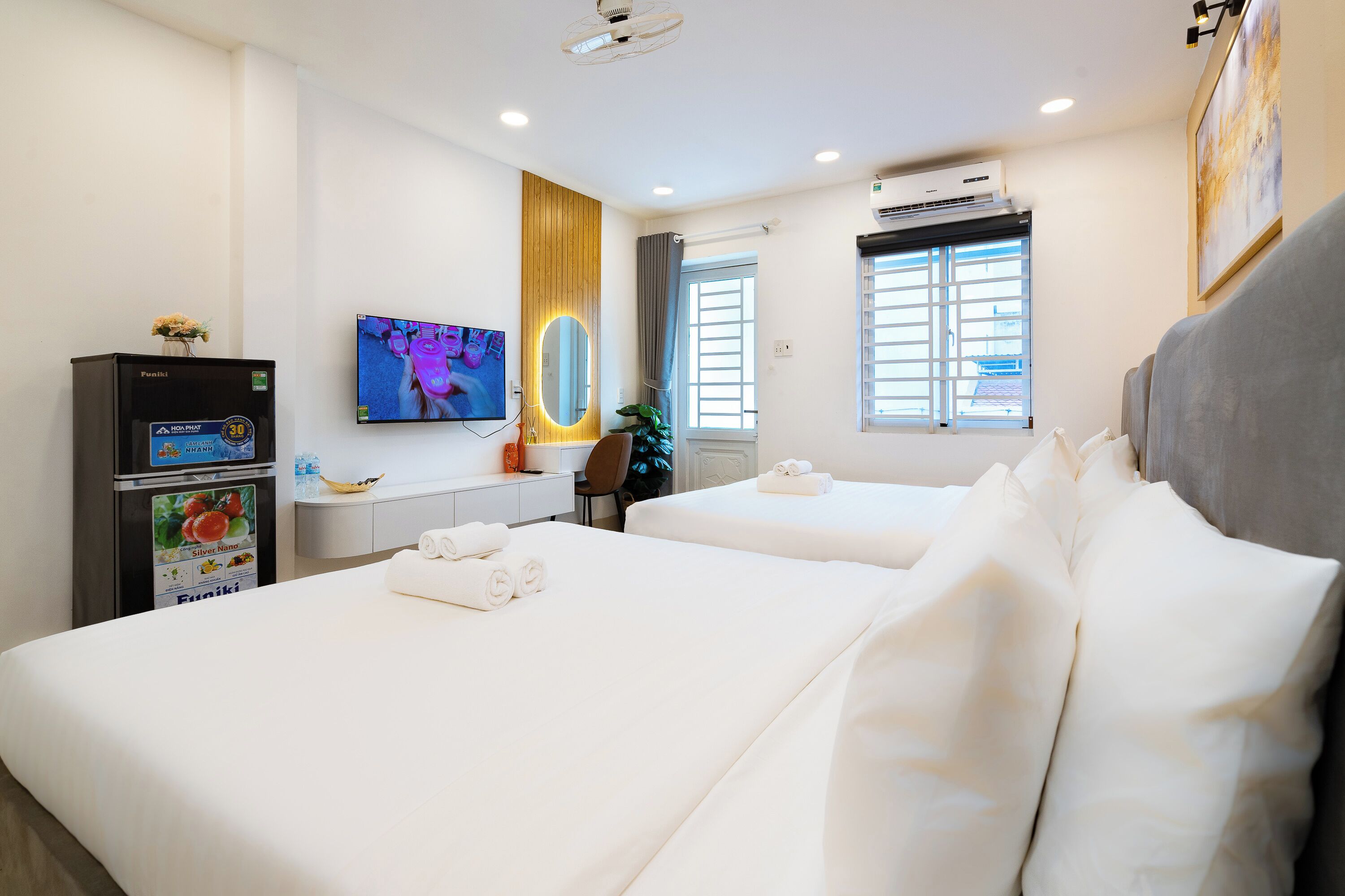 A hotel room with two beds, a TV, a minibar, and a window with curtains.