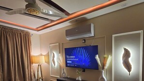 A modern living room with a flat-screen TV, decorative wall art, a ceiling fan, and a mounted air conditioner.